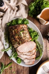 A top down shot of roast pork on a platter with gravy in the background.