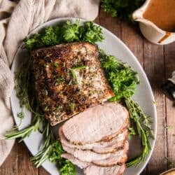 A top down shot of roast pork on a platter with gravy in the background.