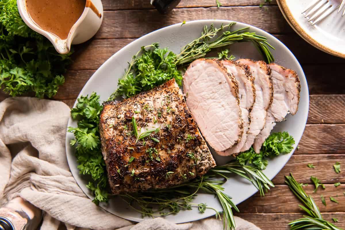 A top down shot of a sliced pork roast on a platter with gravy behind it.