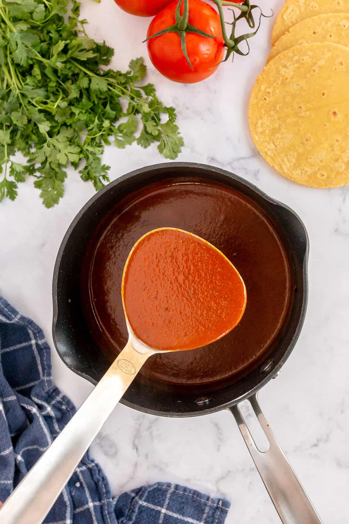 A ladle scoops enchilada sauce from a saucepan.