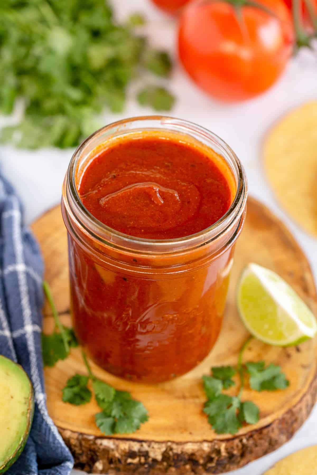 A mason jar full of red enchilada sauce on a wood board.
