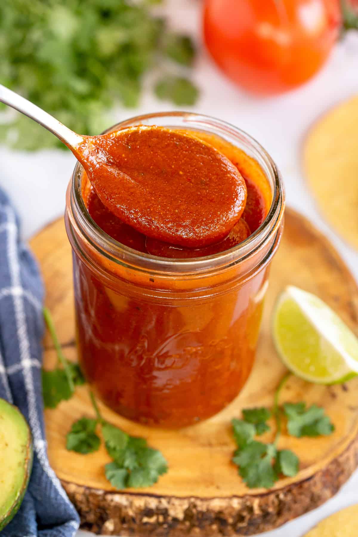 A spoon scoops enchilada sauce from a mason jar.