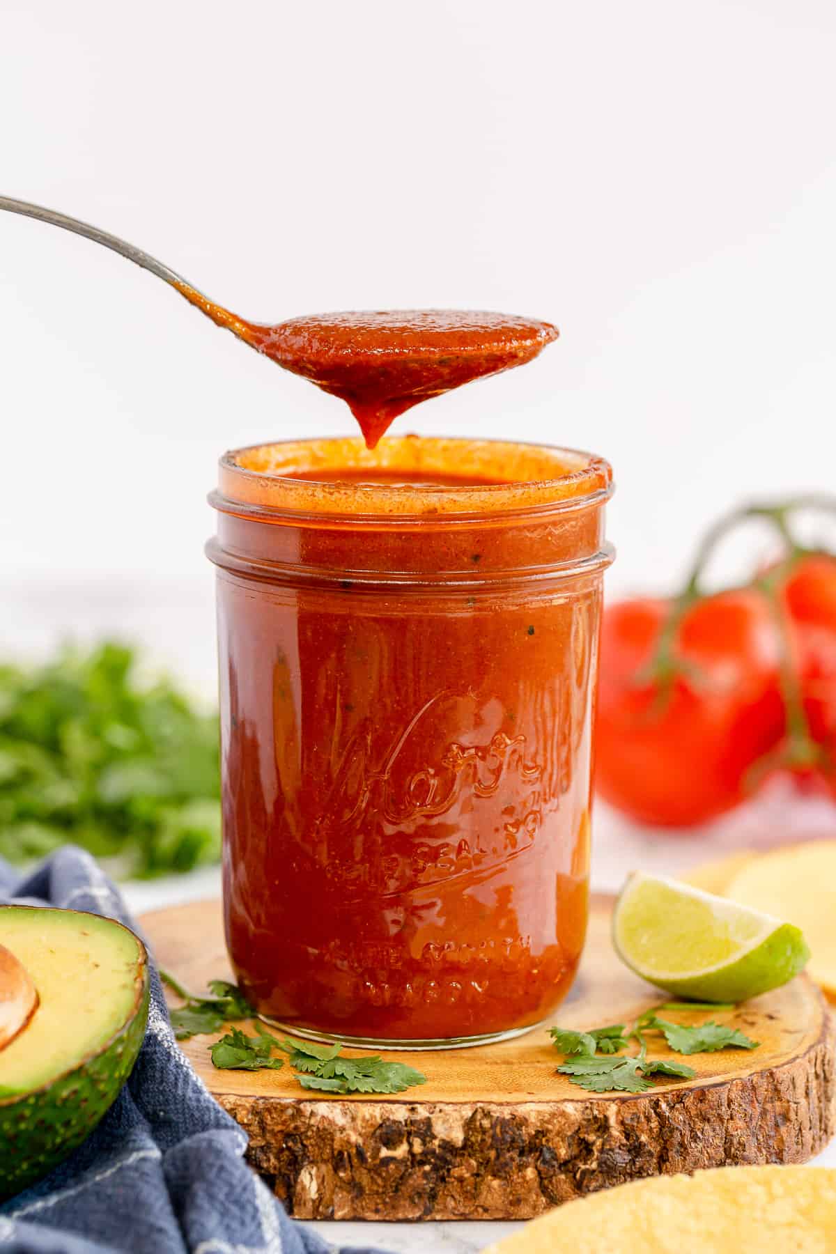 A spoon hovers over a mason jar filled with red enchilada sauce.