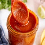 A small wooden spoon pressing into a jar of enchilada sauce.