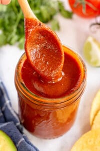 A small wooden spoon pressing into a jar of enchilada sauce.