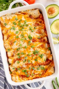 A top down shot of enchiladas topped with red sauce, cheese and green onions in a baking dish.