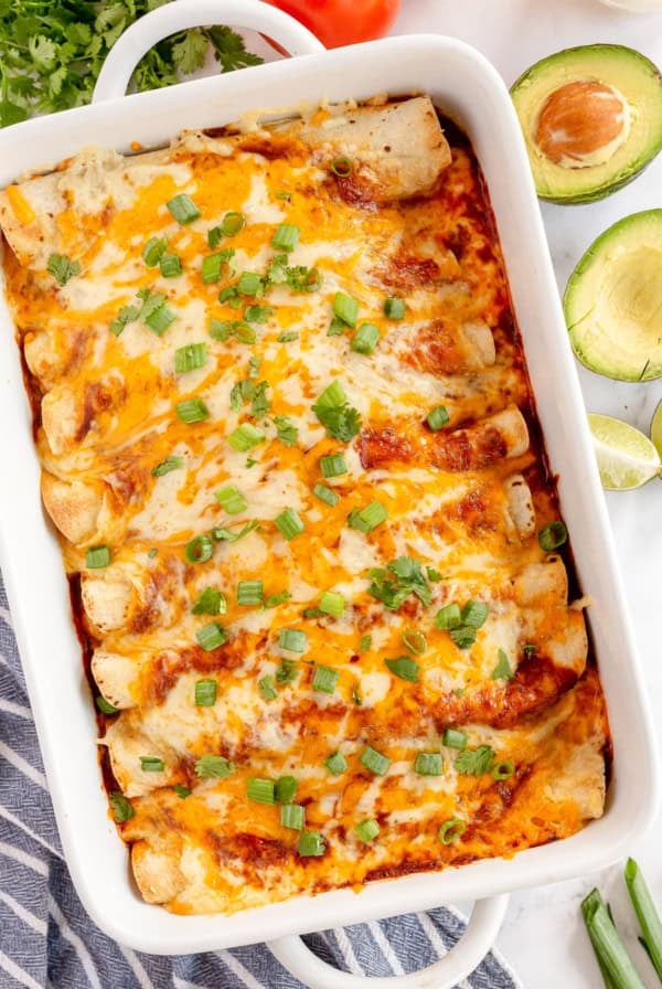 A top down shot of enchiladas topped with red sauce, cheese and green onions in a baking dish.