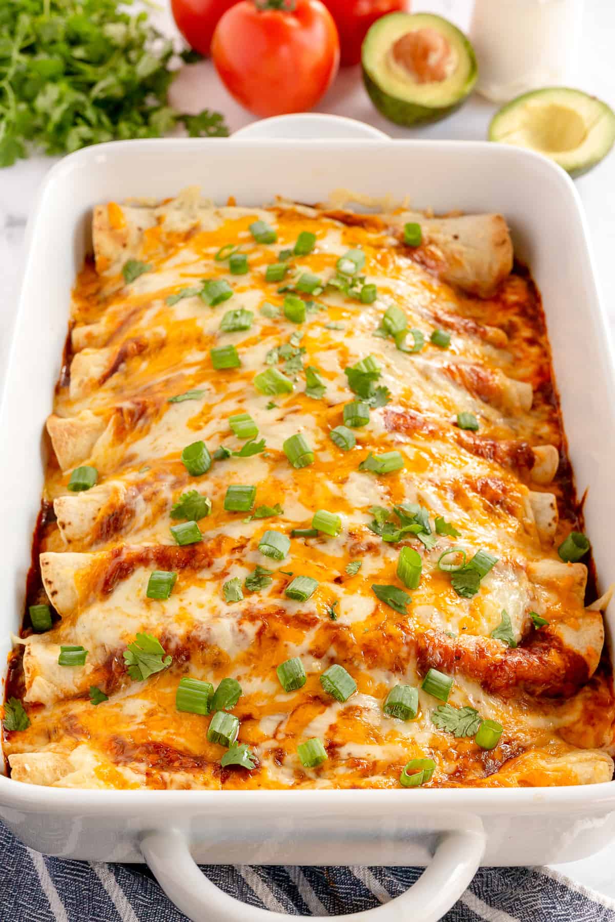 Beef Enchiladas with cheese and green onions in a white baking dish.