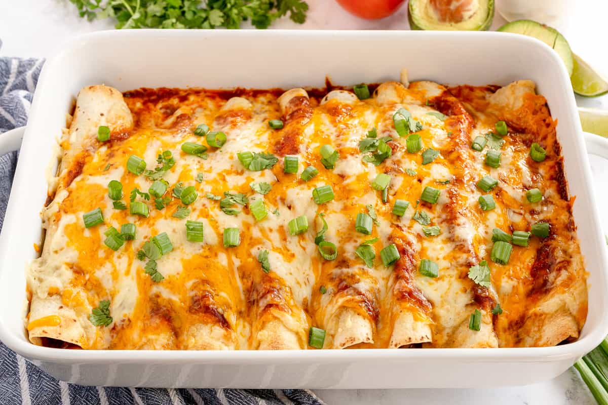 Shredded beef enchiladas in a baking dish with sauce and cheese.