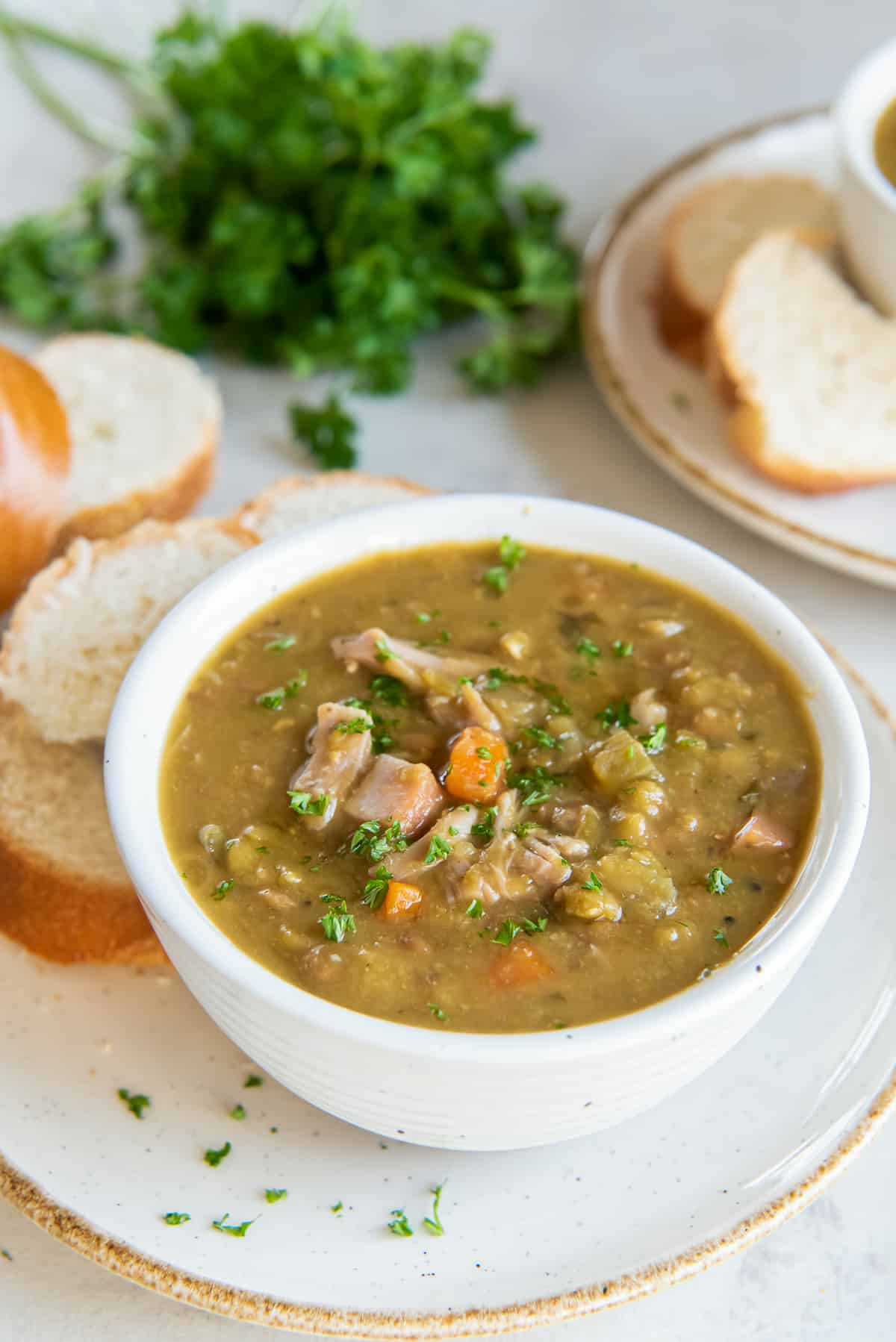 Split pea soup in a white bowl on a plate with sliced bread.