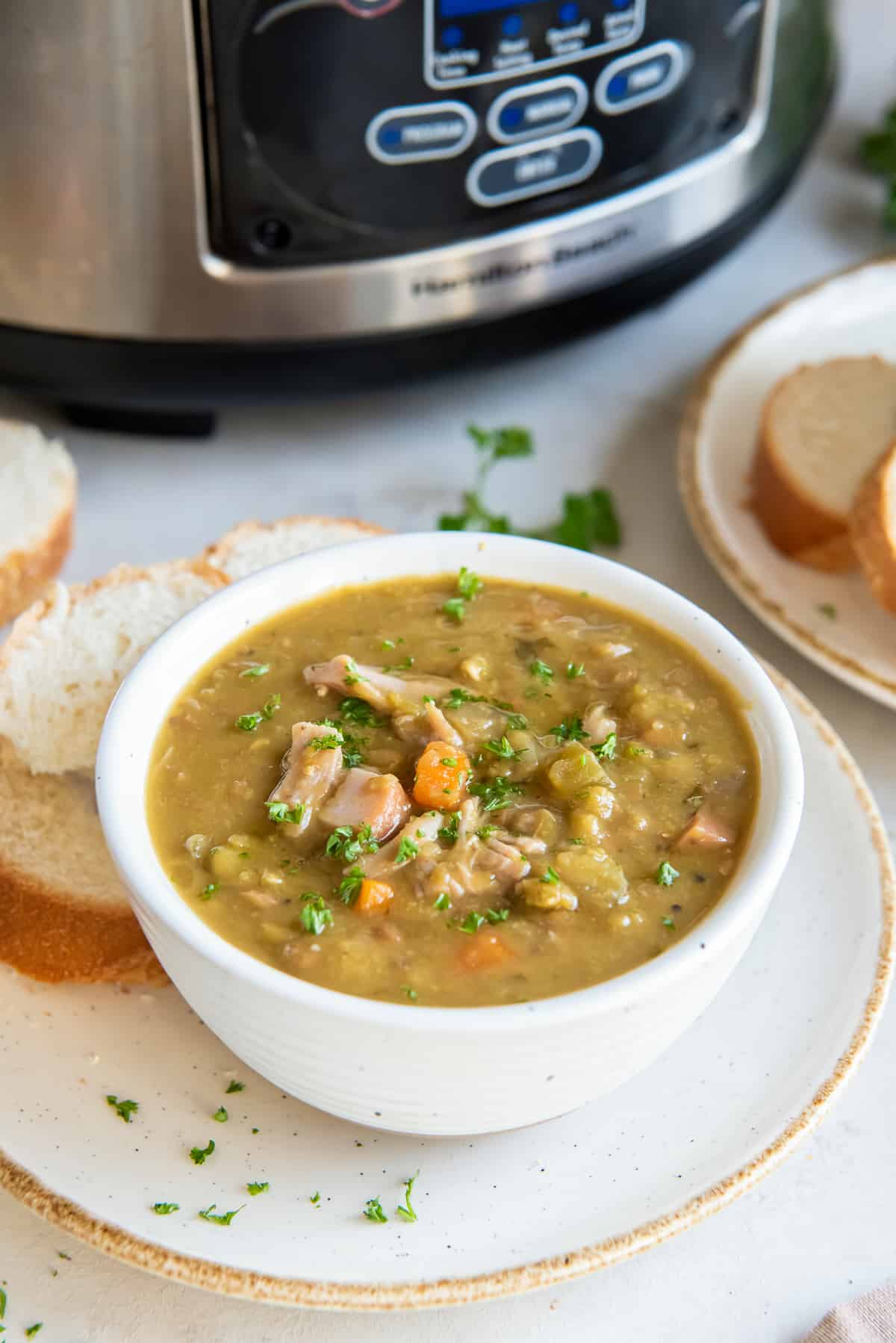 A bowl of split pea soup with ham in front of a slow cooker.