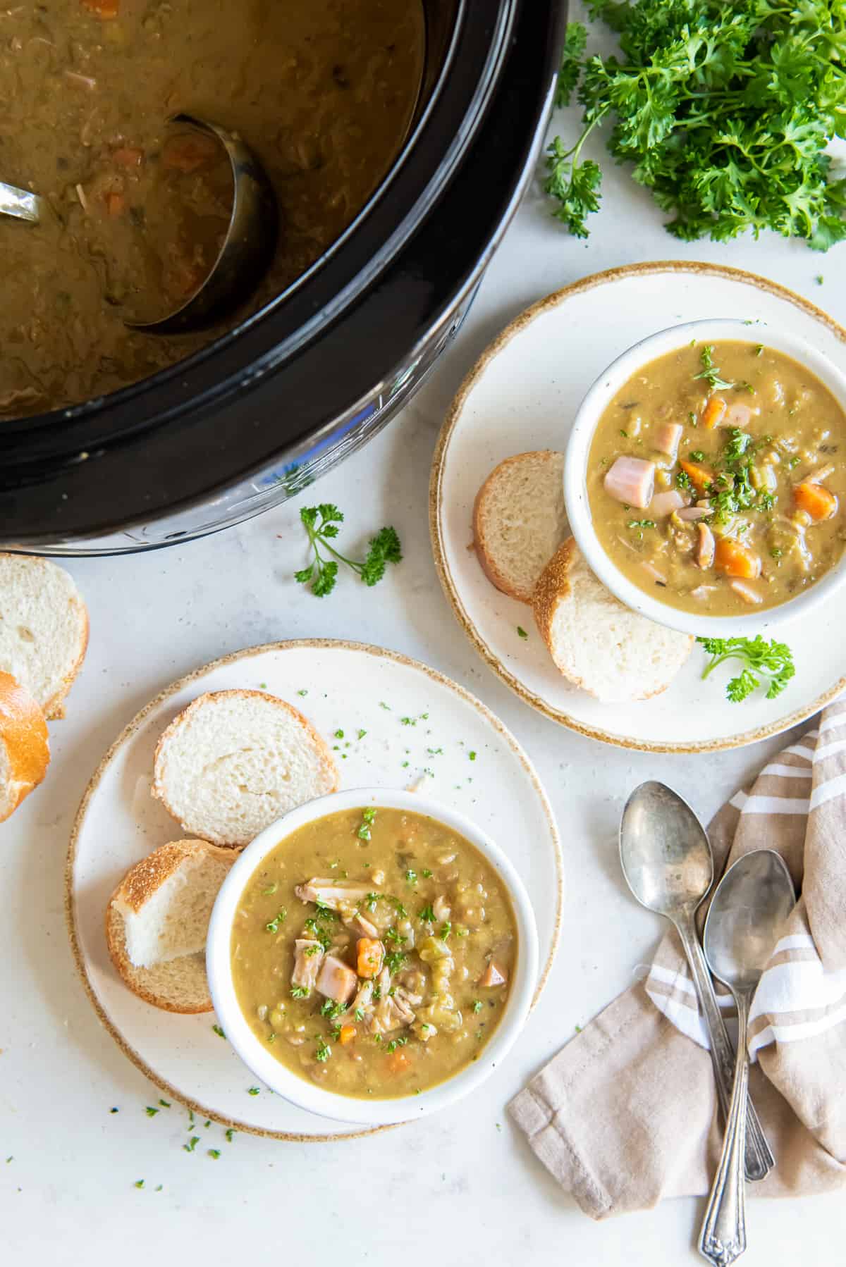A top down shot of two bowls of split pea soup next to a slow cooker.