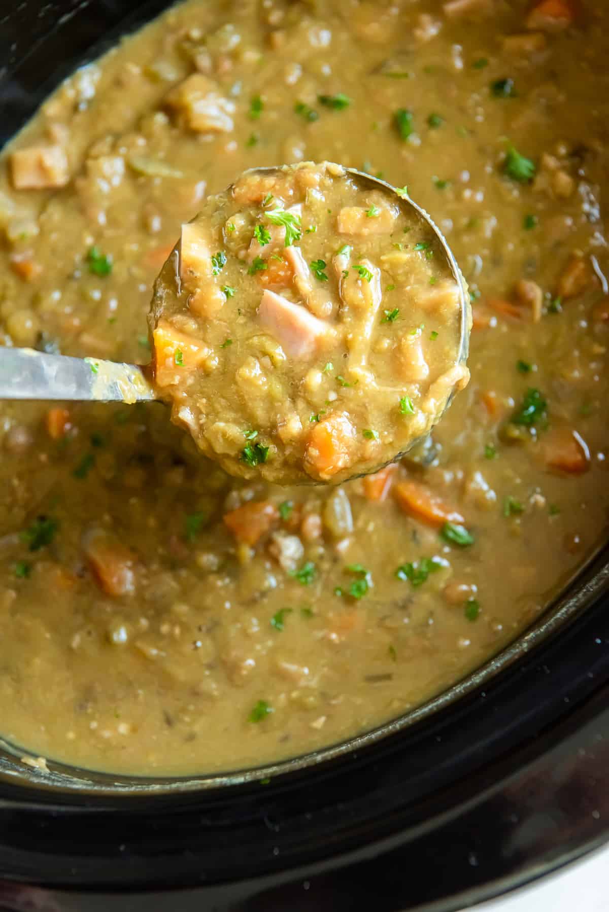 A ladle scoops split pea soup from a slow cooker.