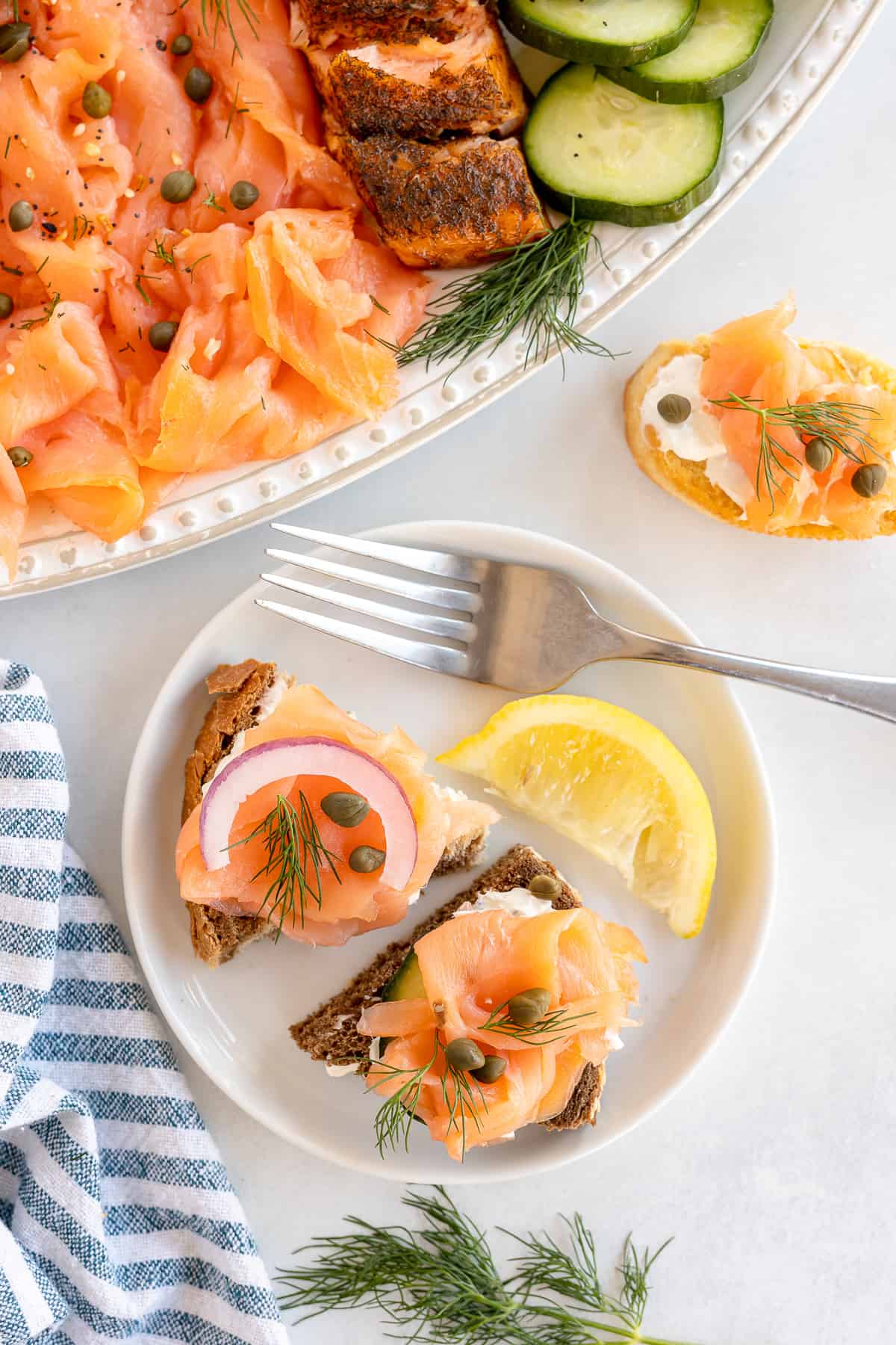 Small breads with cream cheese, smoked salmon, capers and dill on a plate with a lemon wedge.