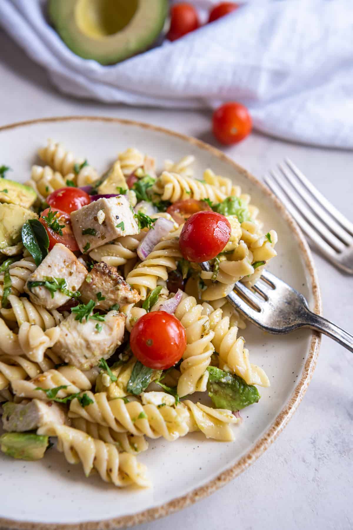 A fork on a plate with chicken avocado pasta salad with cherry tomatoes.