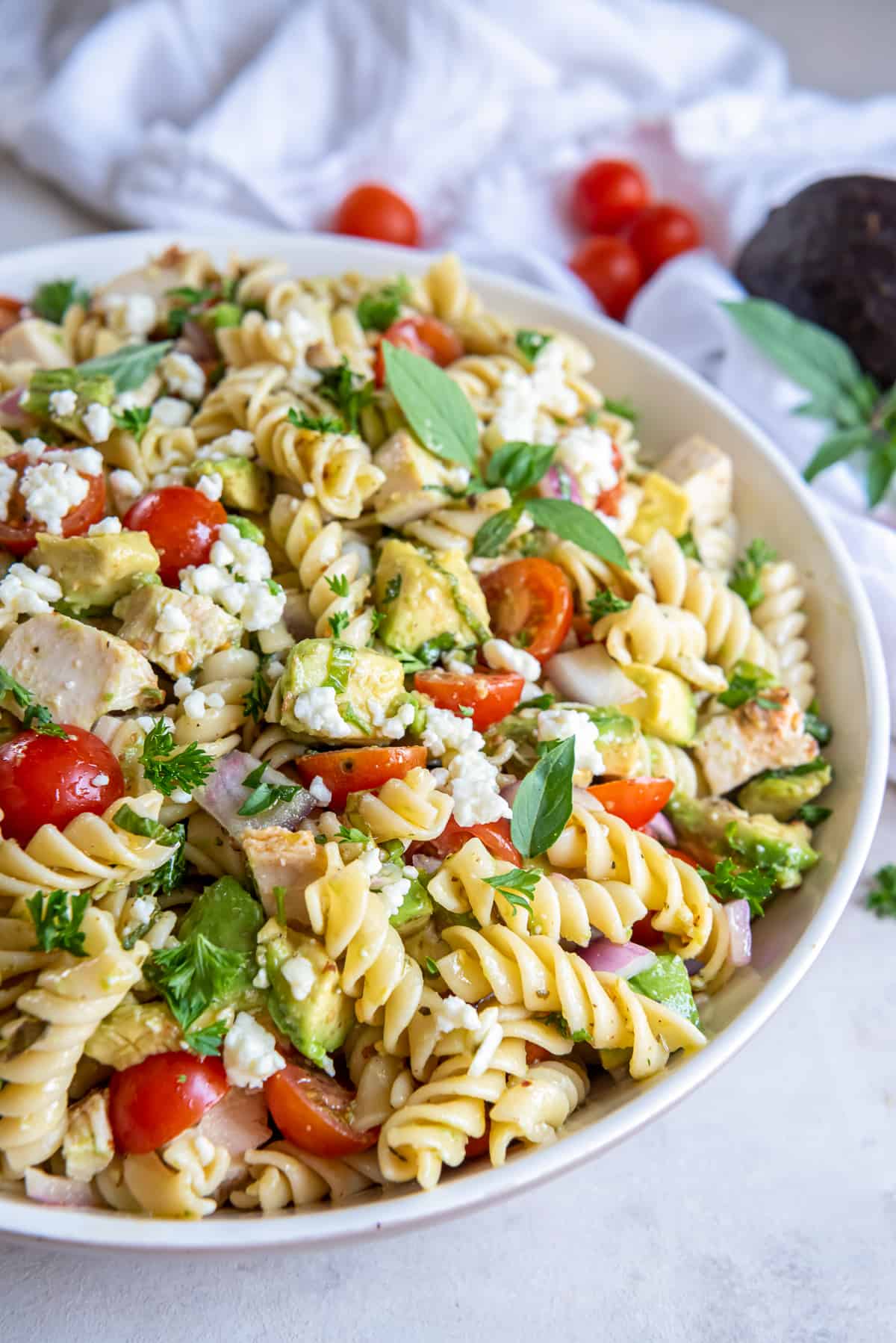 A side view of chicken avocado pasta salad in a white bowl.