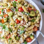 A white bowl filled with chicken avocado pasta salad and salad spoons.