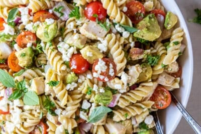 A white bowl filled with chicken avocado pasta salad and salad spoons.