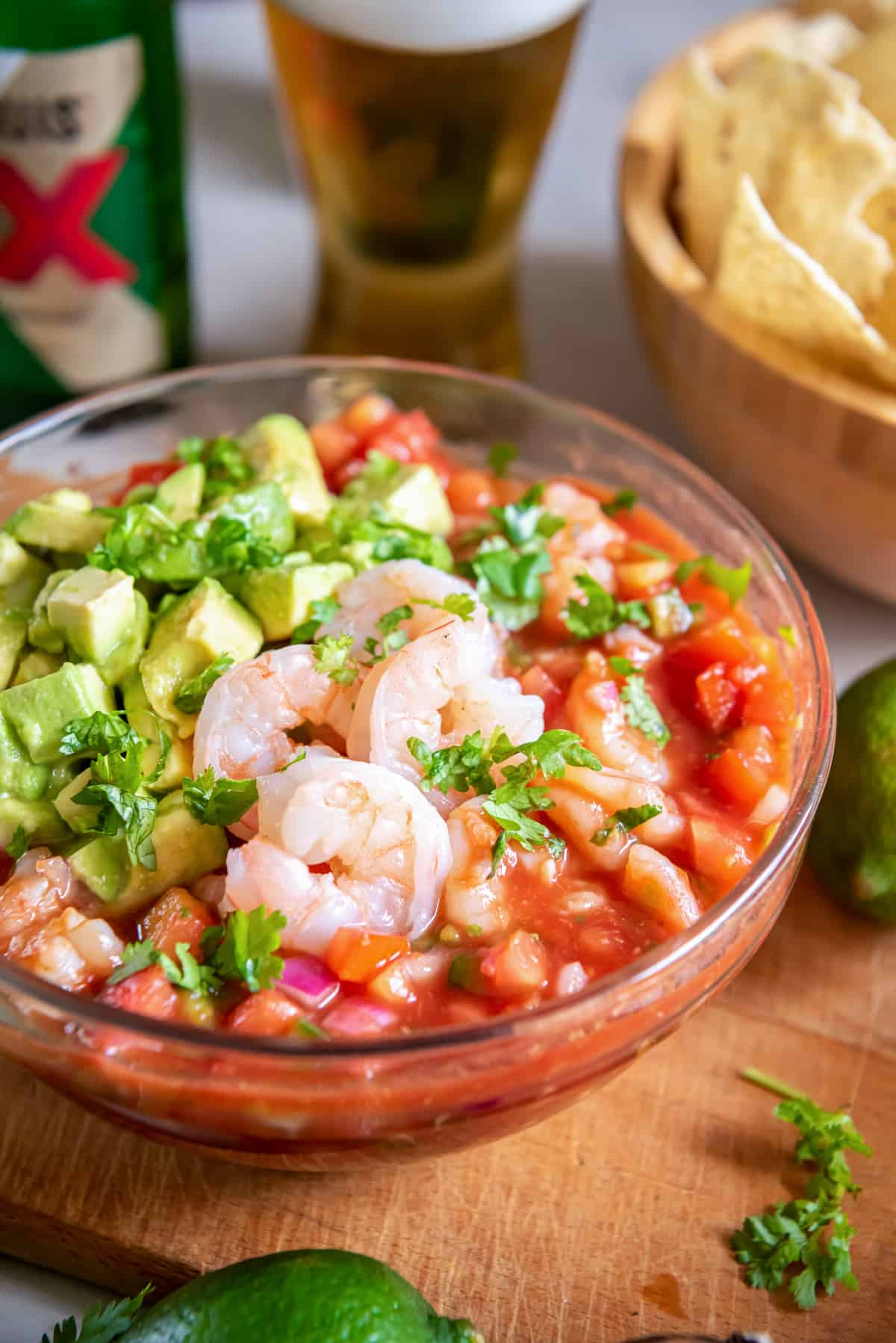 Mexican Shrimp Cocktail with avocado in a serving bowl with beer and tortilla chips in the background.