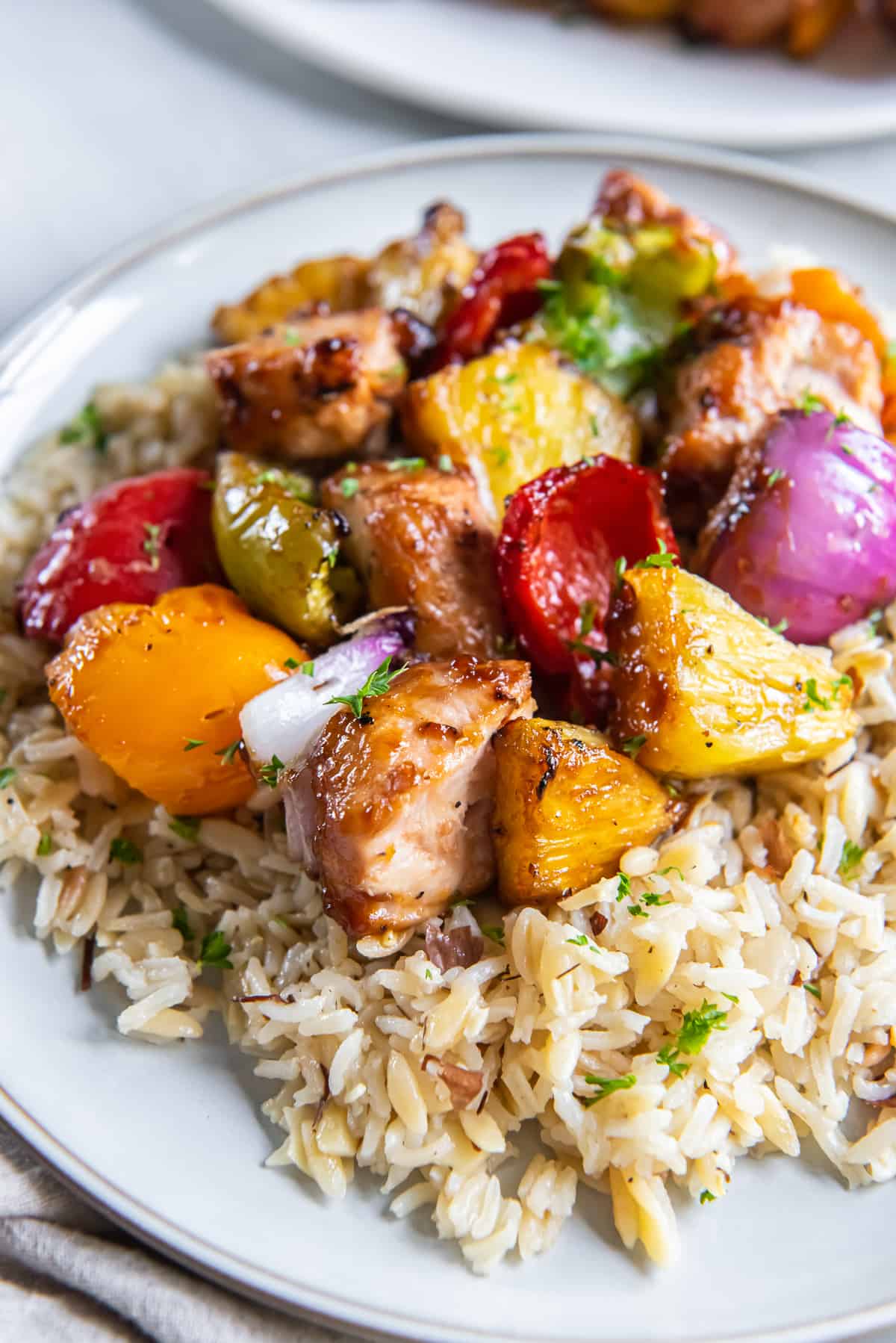 Chicken pineapple and peppers on rice on a white plate.