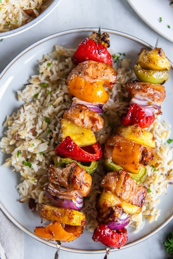 A top down shot of pineapple chicken kabobs on rice on a white plate.