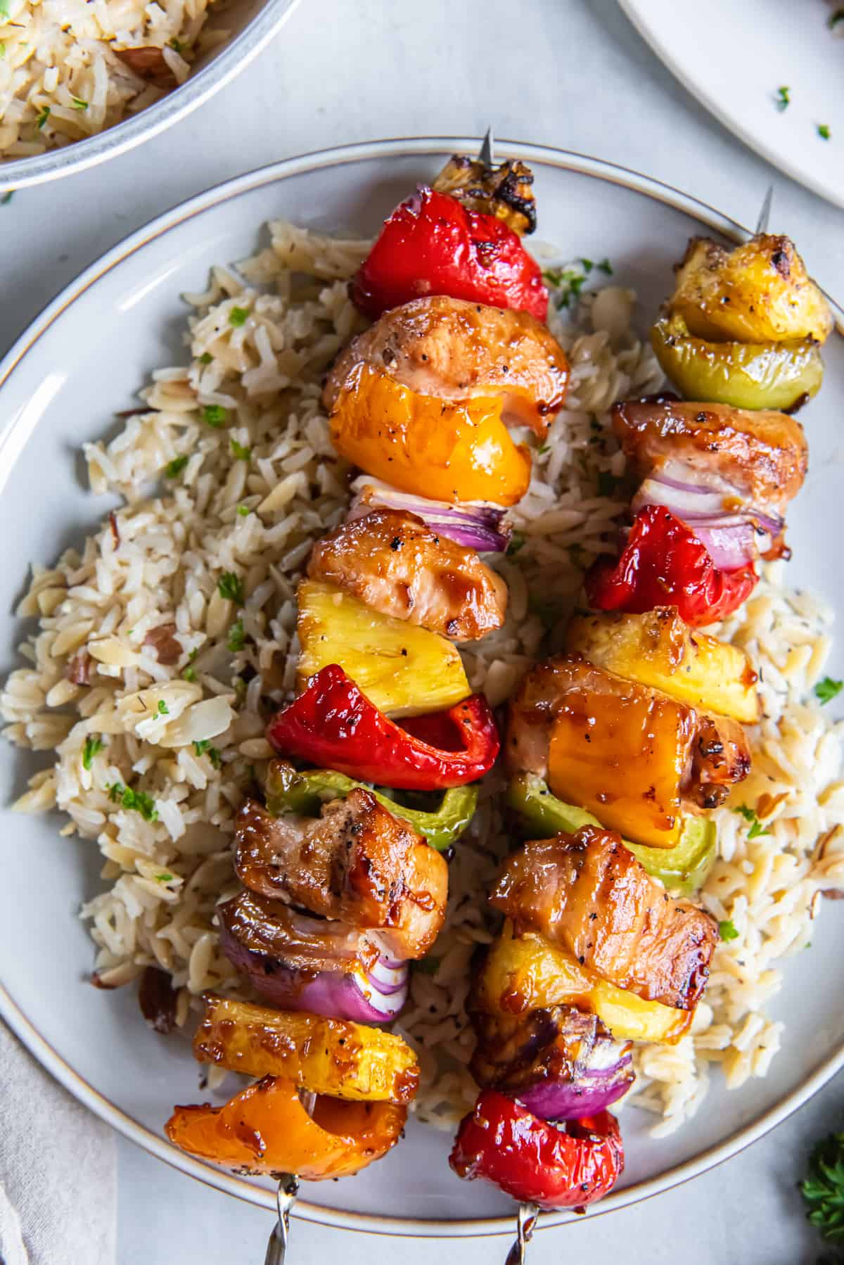 A top down shot of pineapple chicken kabobs on rice on a white plate.