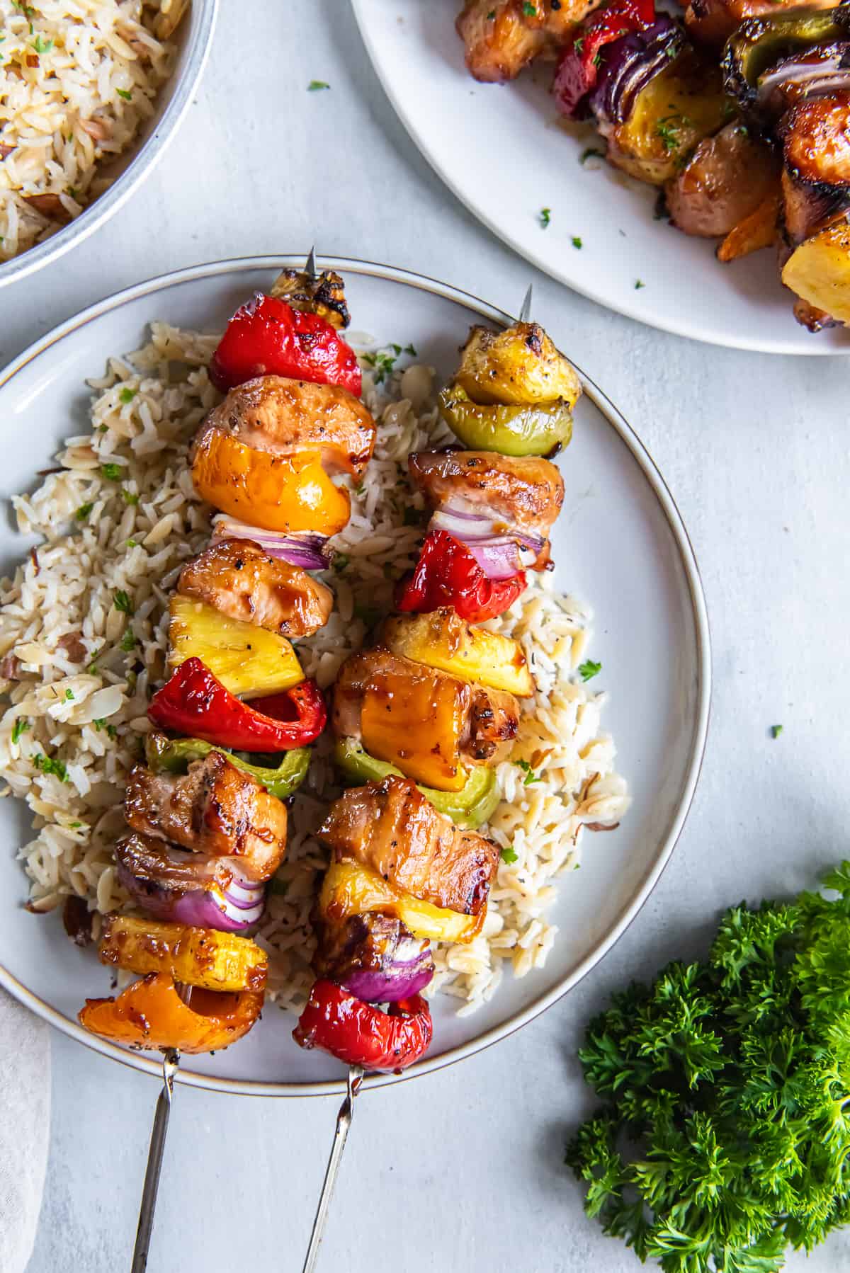 A top down shot of pineapple chicken kabobs on rice on a white plate.