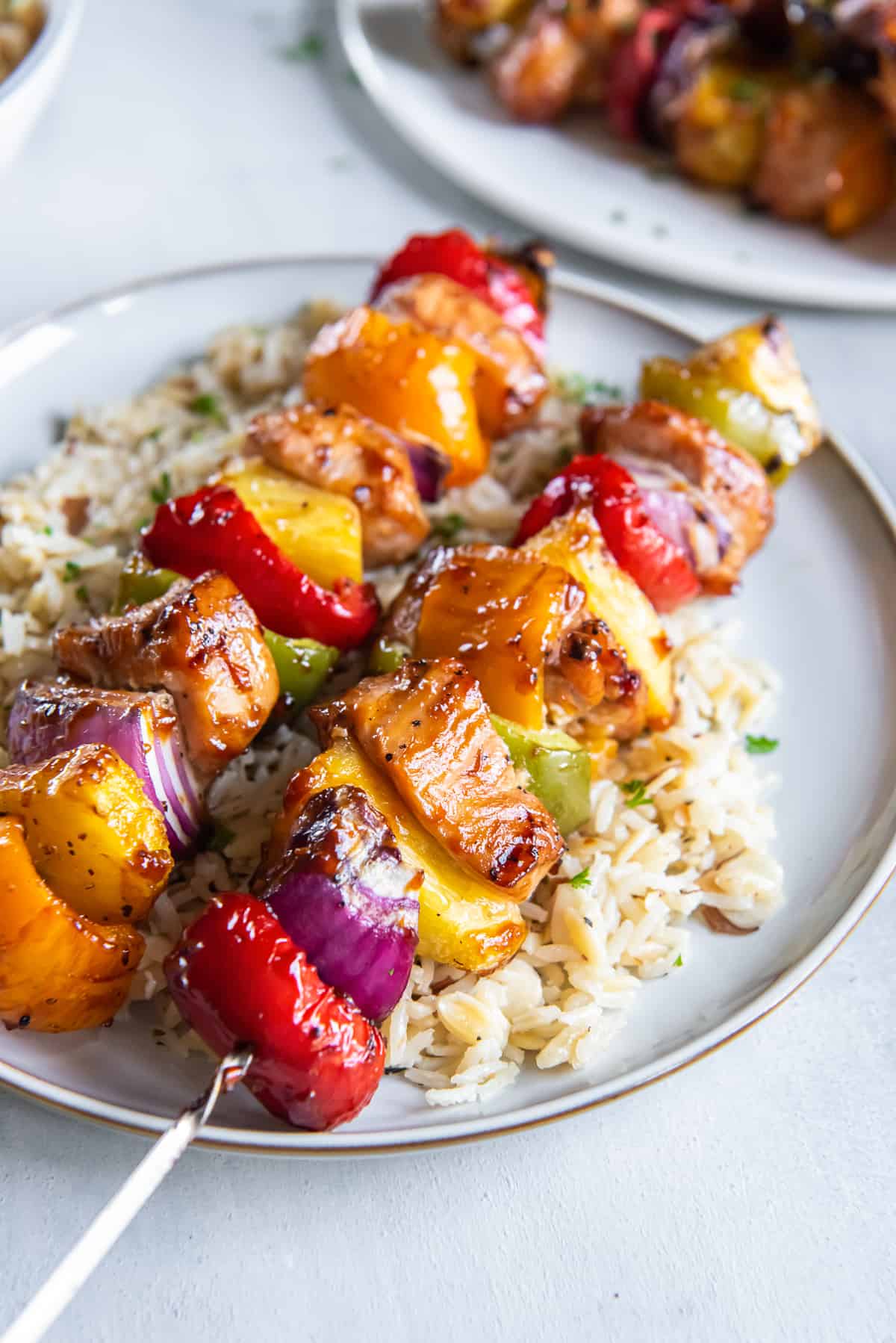 Two hawaiian chicken kabobs on a plate with rice.