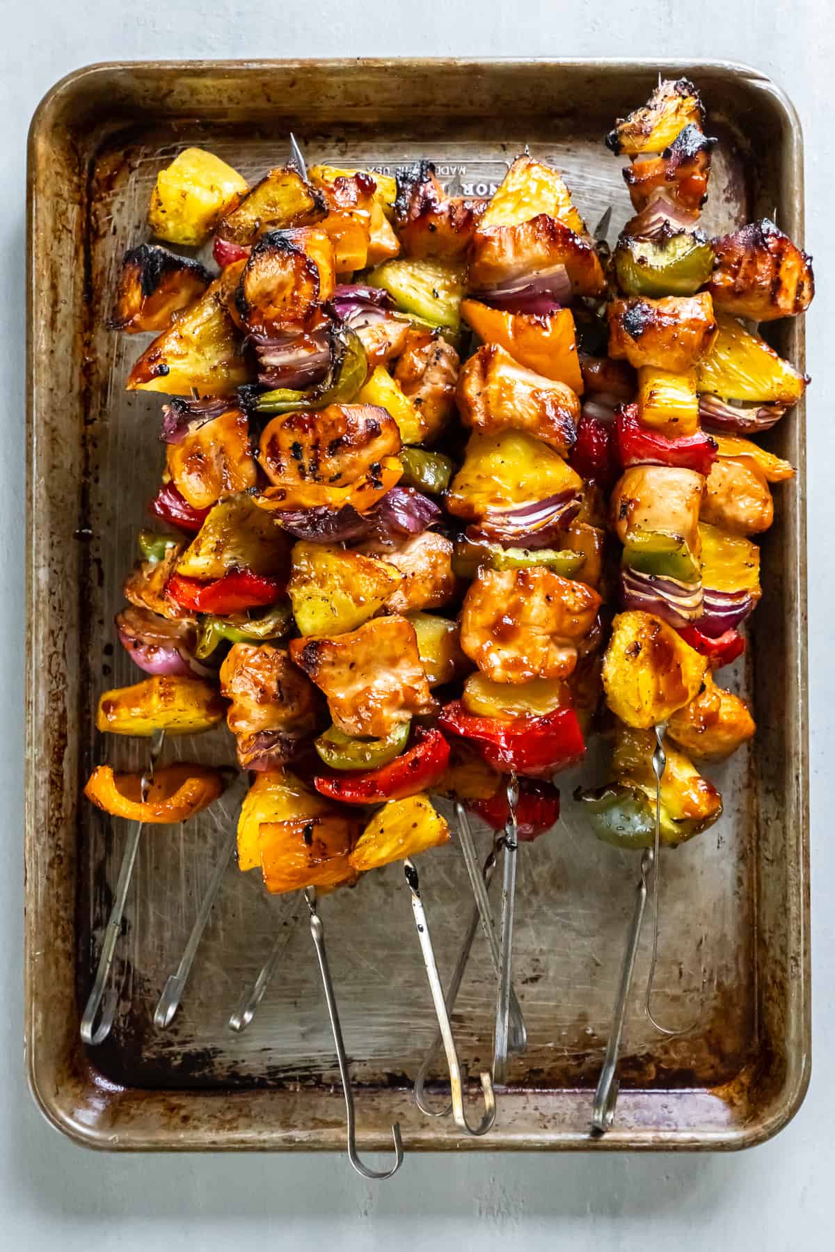 A top down shot of chicken skewers with pineapple on a baking sheet.
