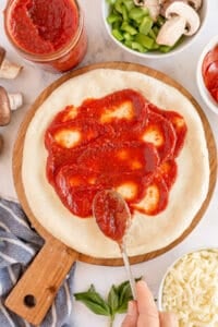 A spoon spreading pizza sauce on pizza crust.