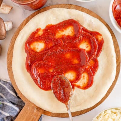 A spoon spreading pizza sauce on pizza crust.