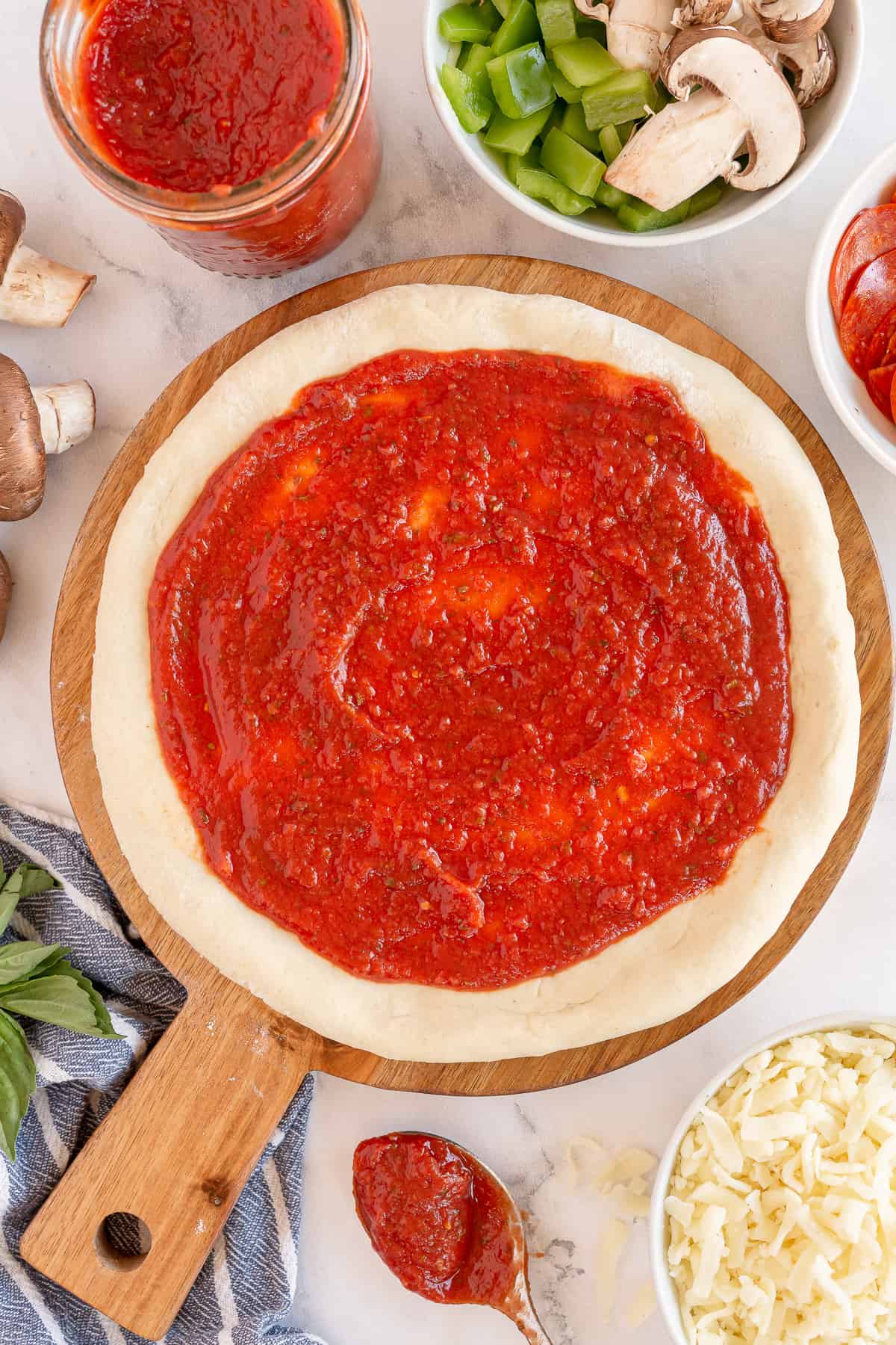 A top down shot of pizza dough topped with pizza sauce.