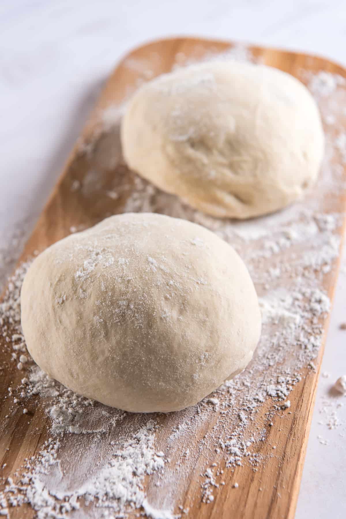 Two balls of pizza dough on a floured board shot from the side.