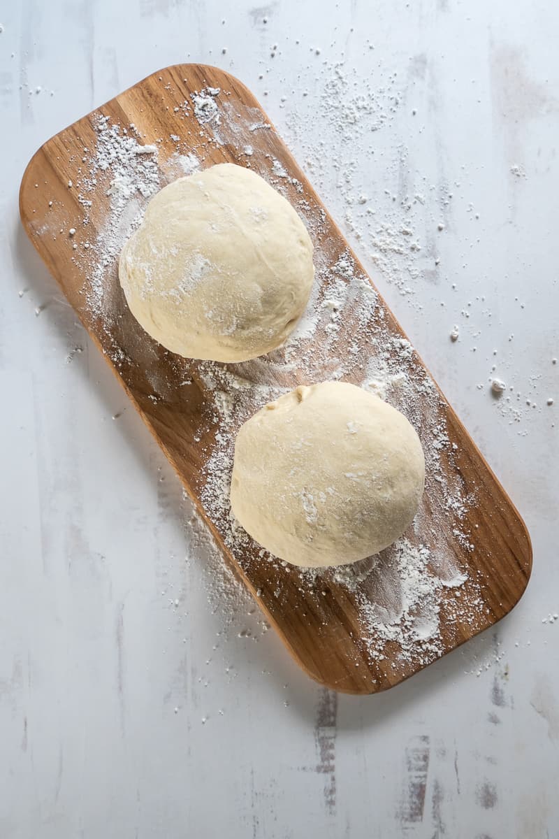 Two balls of pizza dough on a floured board.