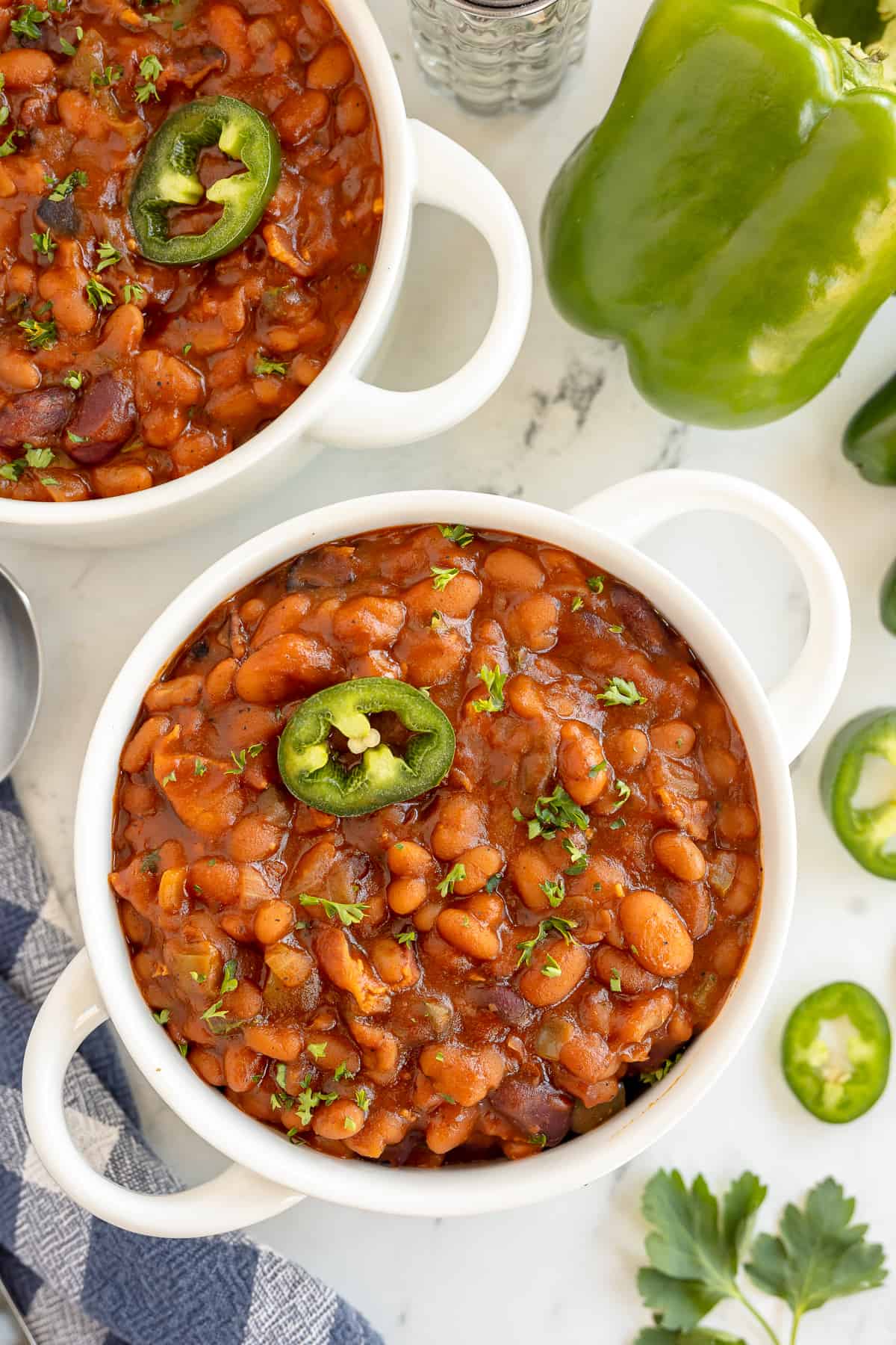 Baked beans with jalapeno in white handled bowls.