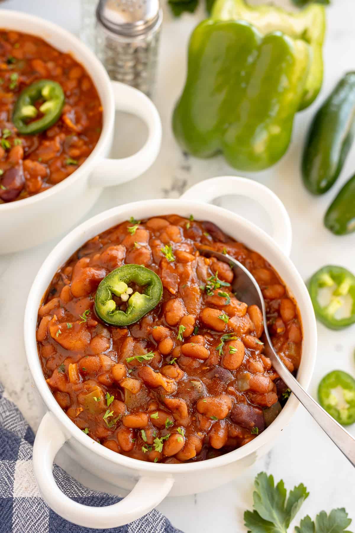 Spicy baked beans in a white handled bowl with a spoon.