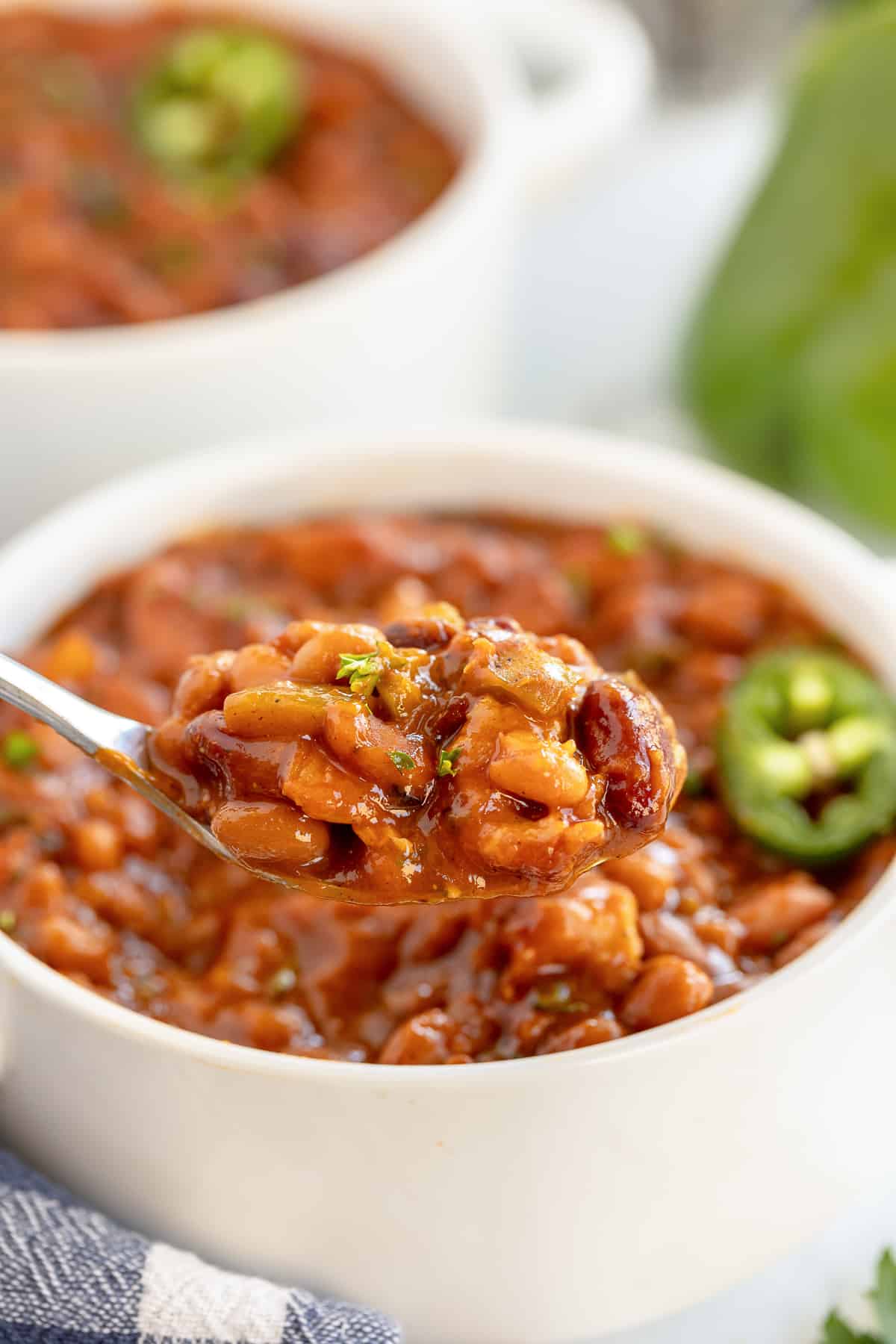 A spoon lifts spicy baked beans from a white bowl.