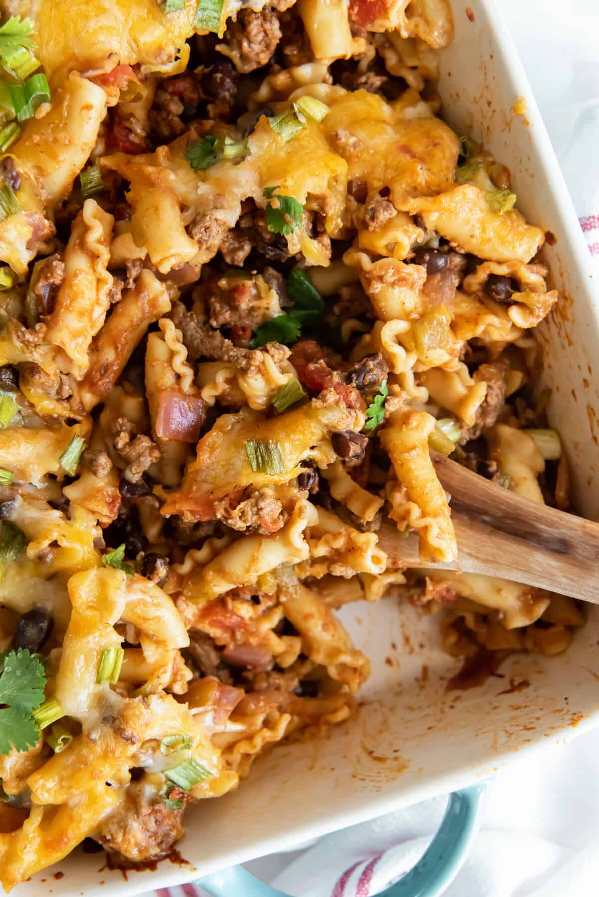 A wooden spoon resting in a casserole dish of taco pasta.