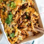 A wooden spoon resting in a casserole dish of taco pasta.