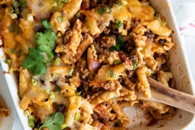 A wooden spoon resting in a casserole dish of taco pasta.