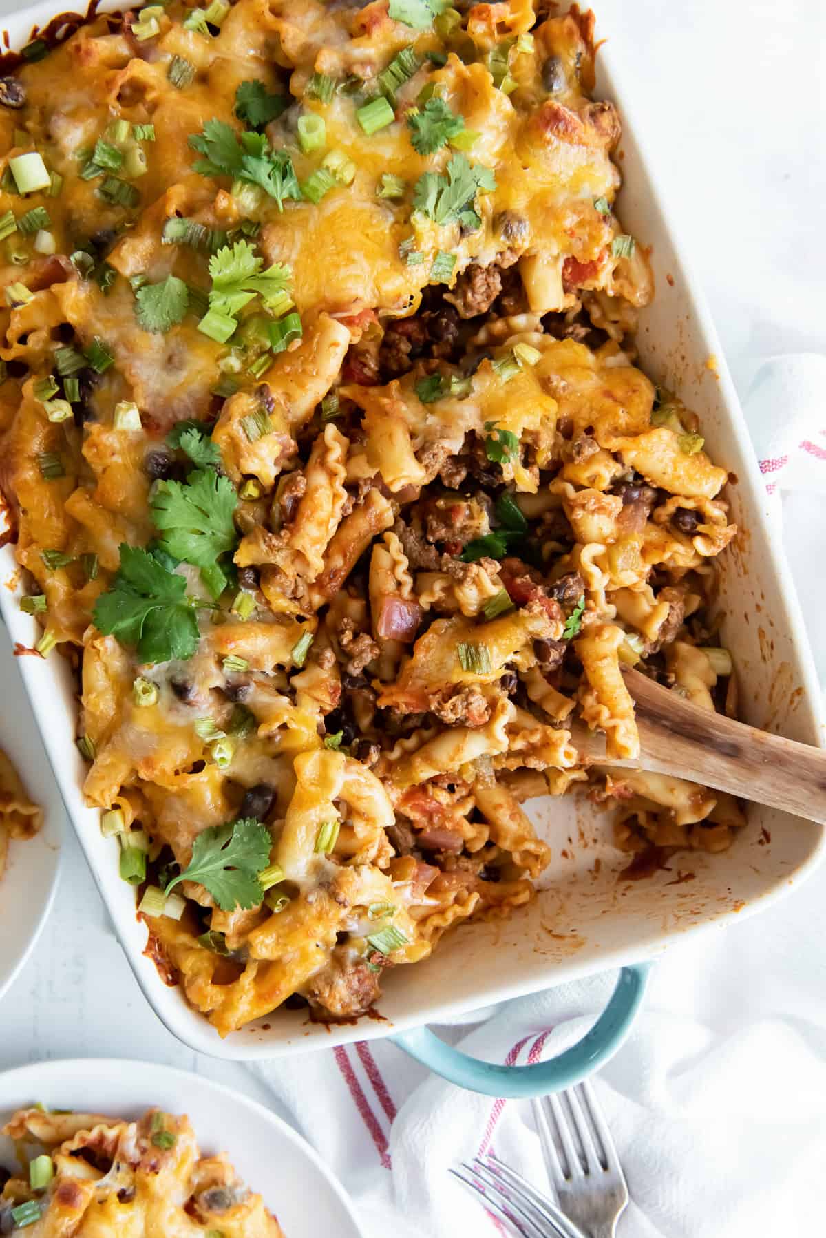 A wooden spoon resting in a casserole dish of taco pasta.