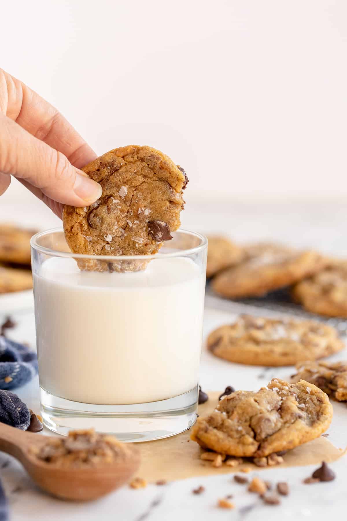 A hand dips a cookie into a glass of milk.