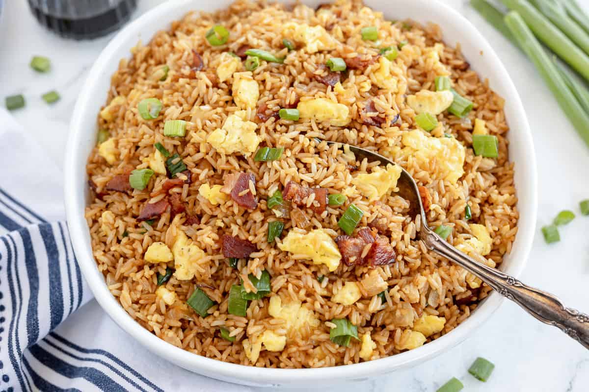 Fried rice with bacon in a white bowl with a spoon.