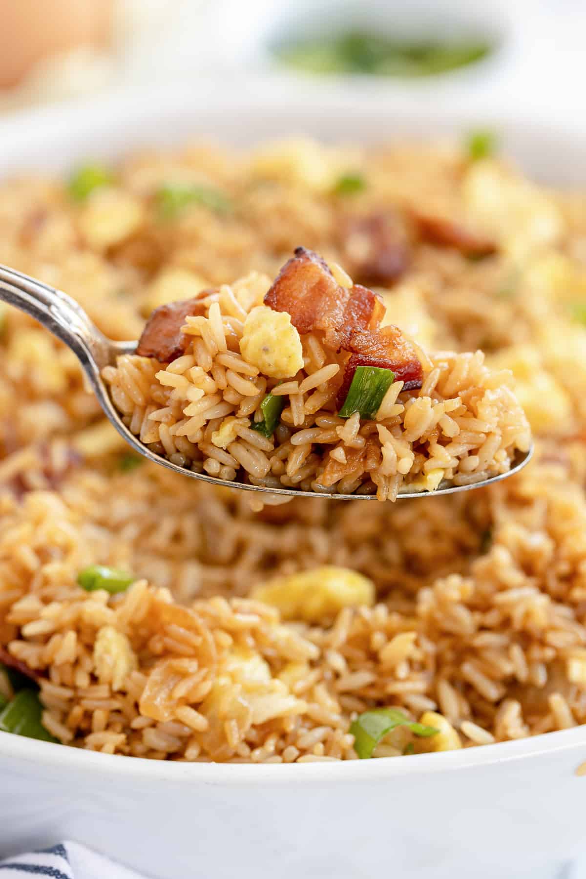 A spoon lifts fried rice from a serving bowl.