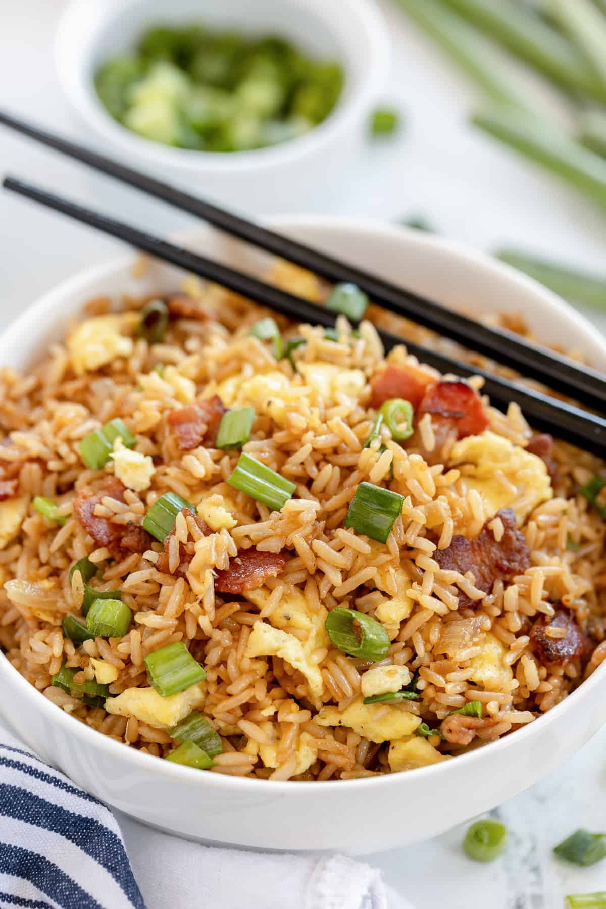 Chopsticks resting on a white bowl filled with fried rice.