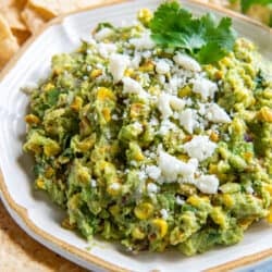 Corn guacamole in a white bowl surrounded by tortilla chips.