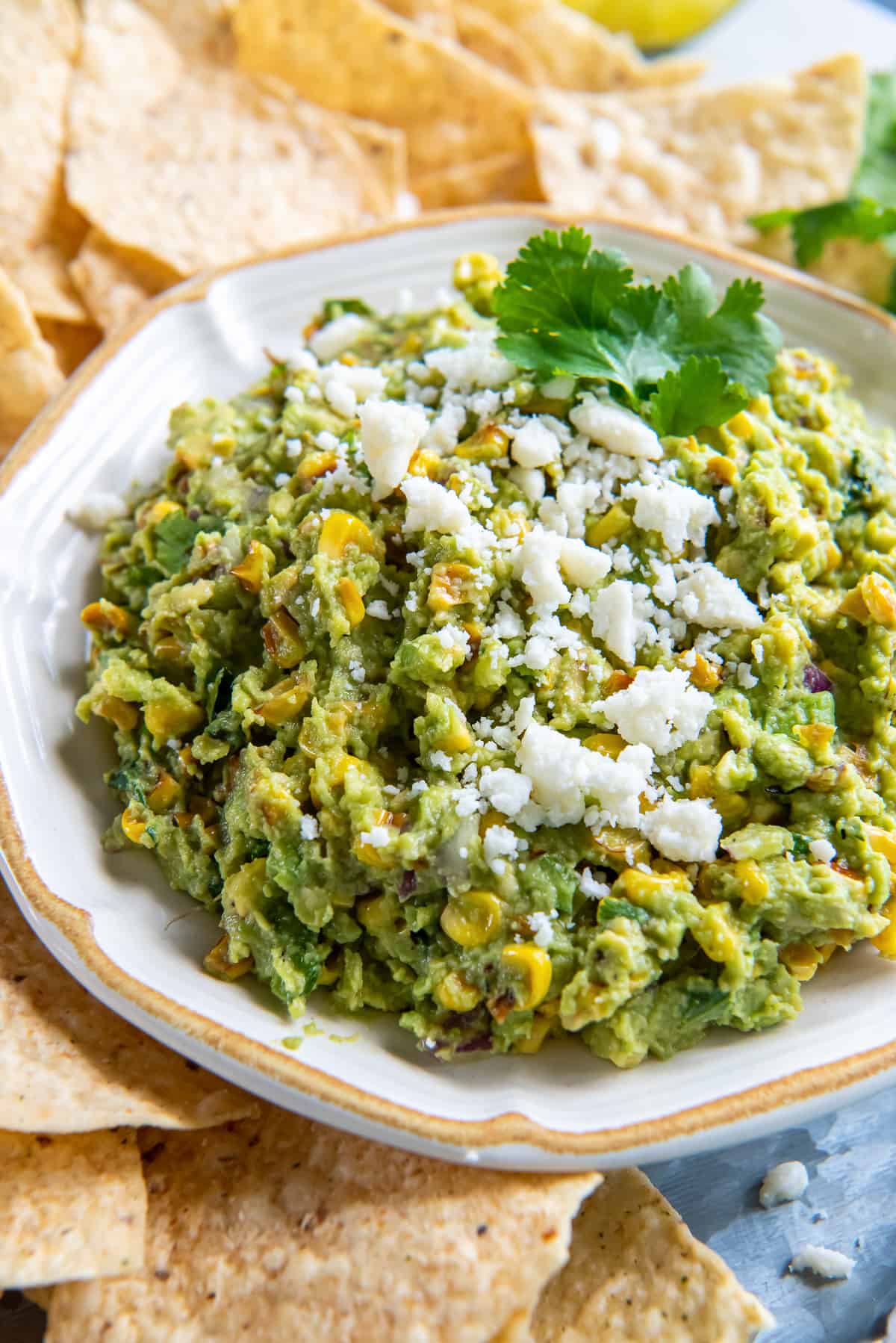 Corn guacamole in a white bowl surrounded by tortilla chips.
