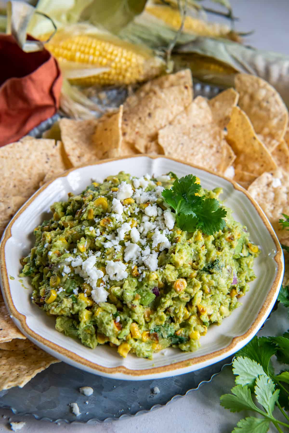 Guacamole with corn topped with cotija in a bowl surrounded by tortilla chips.