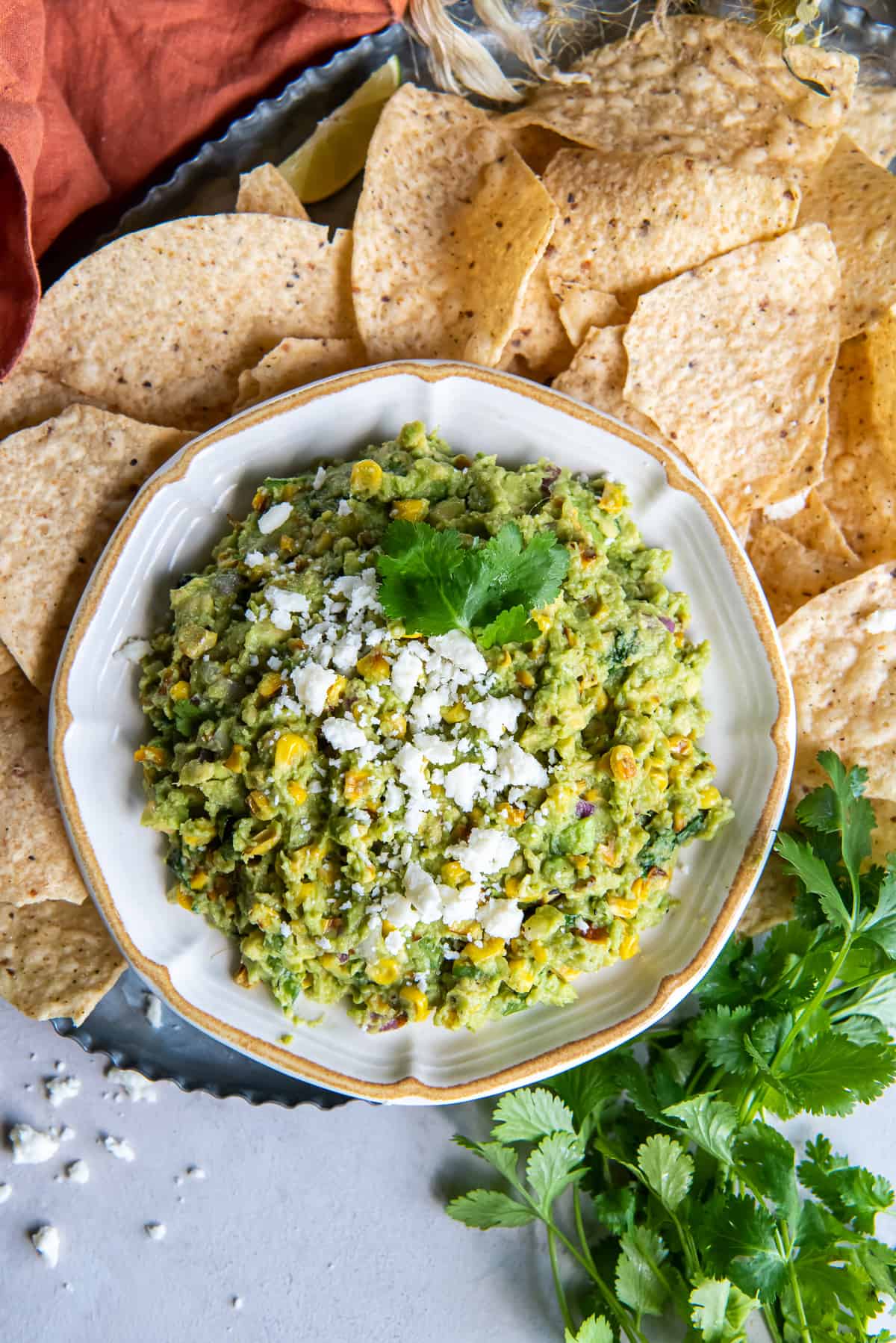 A top down shot of a bowl of corn guacamole surrounded by tortilla chips.