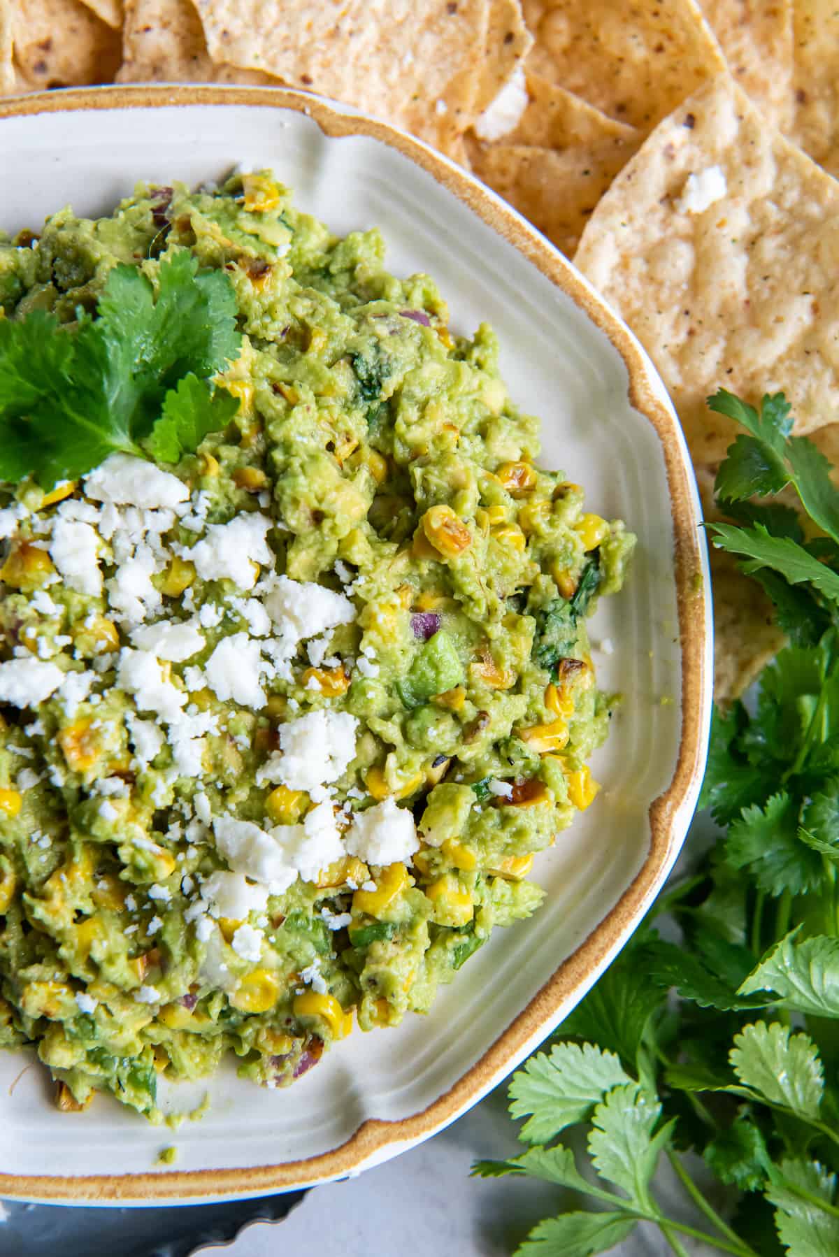 A top down shot of guacamole with corn and cotija cheese in a bowl with cilantro.